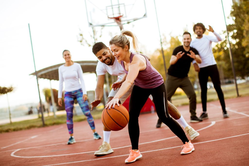 As represented by these adults playing basketball outdoors, a field day featuring sports and games can be an excellent team-building opportunity.
