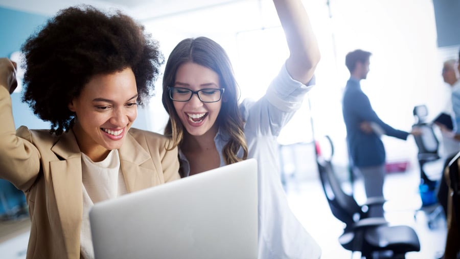 Implementing employee engagement ideas and programs can help boost morale, as represented by this image of two women celebrating success while looking at a laptop.